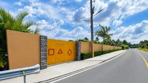 A road with a yellow wall featuring geometric shapes and a metal barrier. - Villa la Santa, Higüey - La Altagracia (Higüey)