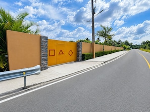 Carretera con un muro amarillo que presenta formas geométricas y una barrera metálica.