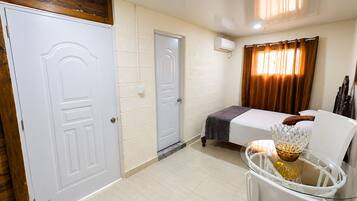 Una habitación de hotel con cama, un área de descanso con una mesa de vidrio y una ventana con cortinas.