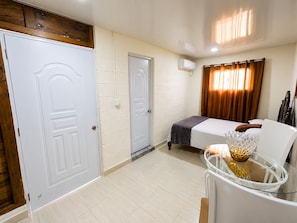 A hotel room with a bed, a seating area with a glass table, and a window with curtains.