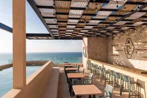 An outdoor seating area with tables and chairs, a pool, and a view of the ocean. - Unforgetable Luxury Beachfront Condo with Ocean View and Rooftop (Sisal)