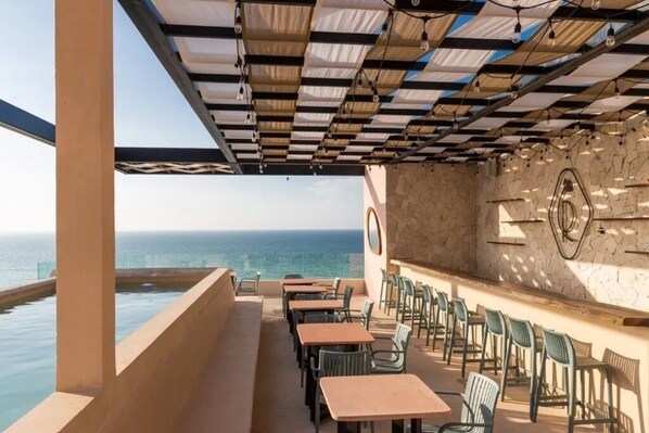 An outdoor seating area with tables and chairs, a pool, and a view of the ocean.