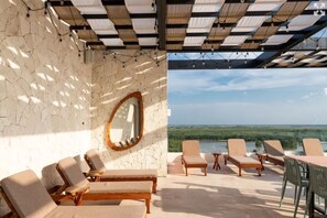 A terrace with lounge chairs, a view of greenery, and a stone wall with a mirror.