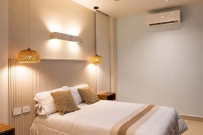 A bedroom with a bed, two bedside tables, a wall-mounted air conditioner, and two hanging lamps.