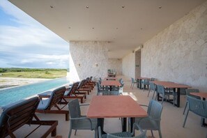 A dining area with tables and chairs, a pool, and a stone wall.