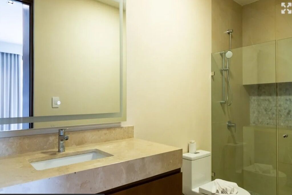 A bathroom with a sink, mirror, toilet, and glass-enclosed shower.