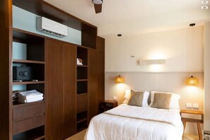 A bedroom with a bed, wooden wardrobe, bedside lamps, and an air conditioning unit.