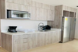 A modern kitchen with wooden cabinetry, a built-in microwave, a stainless steel refrigerator, and a coffee maker on the counter.