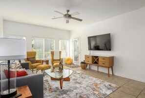 Ein modernes Wohnzimmer mit Sofa, Ohrensessel, Couchtisch und Fernseher an der Wand.