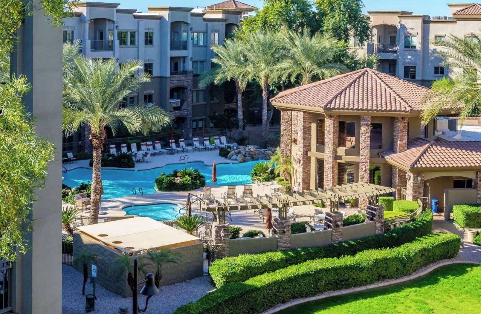 A resort with a swimming pool, palm trees, and a building with a tiled roof.