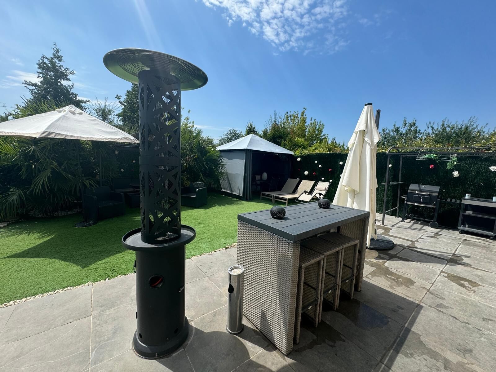 A patio with a table, chairs, a grill, and a decorative lamp.