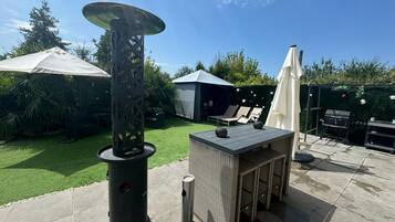 A patio with a table, chairs, a grill, and a decorative lamp.