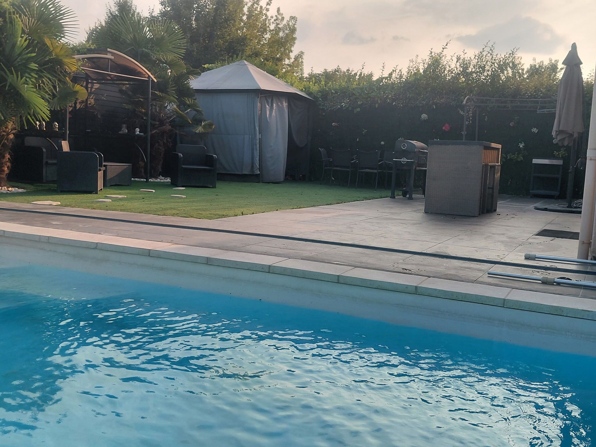 Una piscina con una zona de estar cubierta y sillas reclinables.