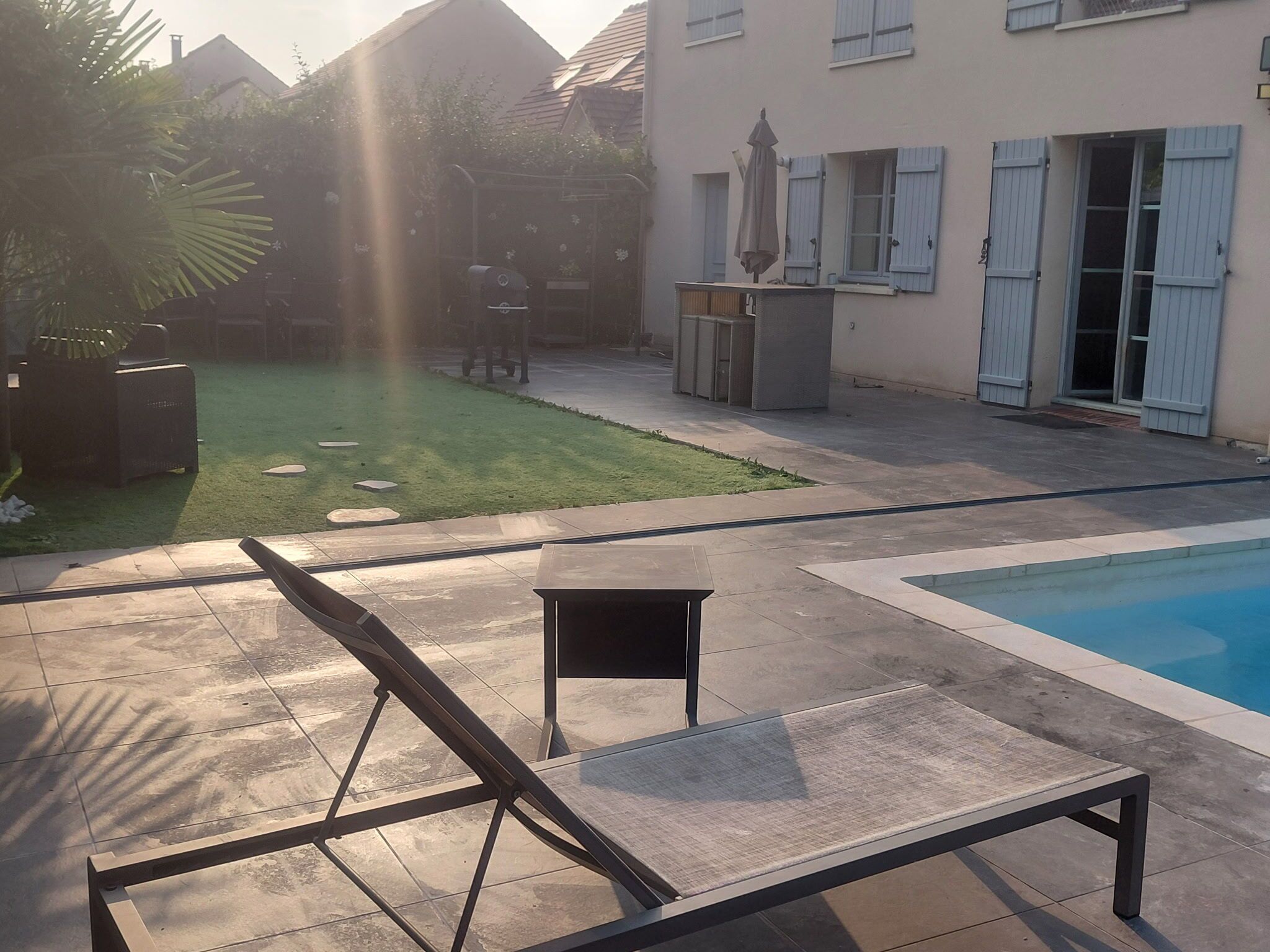 Un área junto a la piscina con una silla de descanso, una mesita y una parrilla.
