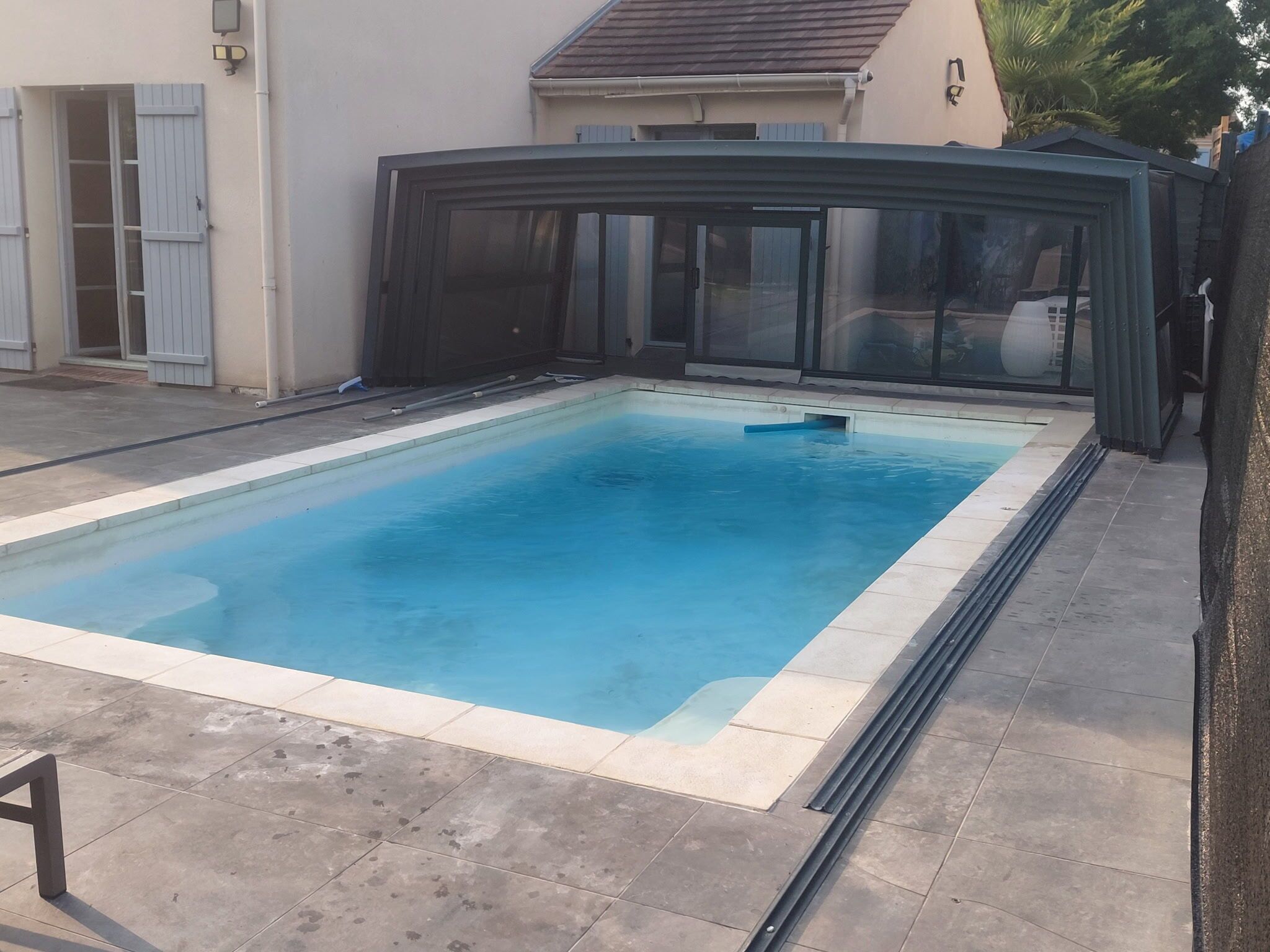 Ein rechteckiger Swimmingpool mit einer klaren blauen Wasseroberfläche, umgeben von einer gefliesten Poolterrasse.