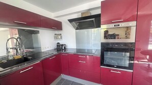 A kitchen with red cabinets, a black countertop, a coffee maker, and a stainless steel sink. - House with a pool and tropical garden (Bruyères-sur-Oise)