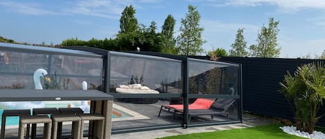 A patio area with a pool, outdoor furniture, and a glass enclosure.