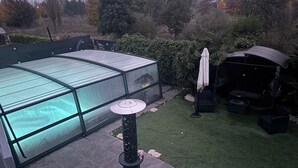 A covered patio area with a glass enclosure, a round table, and a grill. - House with a pool and tropical garden (Bruyères-sur-Oise)