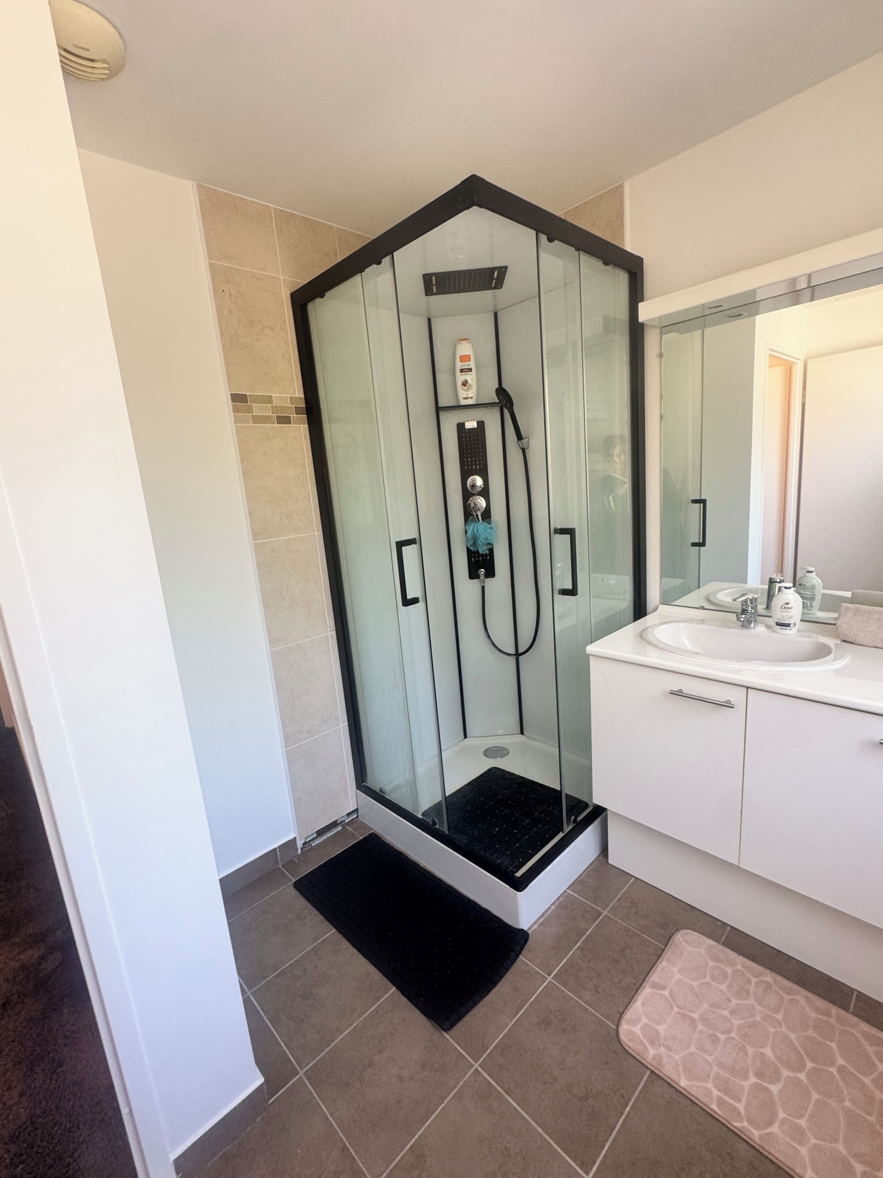 Een moderne badkamer met een douchecabine van glas, een witte wastafel en een spiegel.