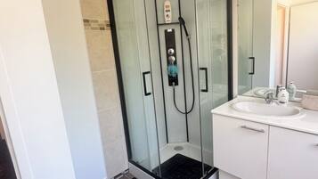 Een moderne badkamer met een douchecabine van glas, een witte wastafel en een spiegel.