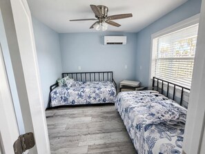 Un dormitorio con dos camas, ventilador de techo, equipo de aire acondicionado y ventana con persianas.