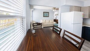 A dining area with a wooden table and chairs, a kitchen with a white refrigerator, and a living room with a beige sofa. - Beautiful spacious upgraded 2-bedroom condo sleeps 8 (St. Pete Beach)
