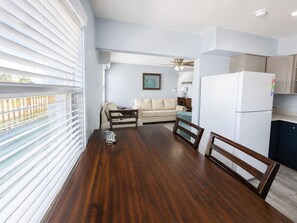 Ein Essbereich mit Holztisch und -stühlen, eine Küche mit weißem Kühlschrank und ein Wohnzimmer mit beiger Couch.