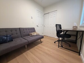 Ein Zimmer mit einem grauen Sofa, einem kleinen Tisch mit Stuhl und weißen Türen.