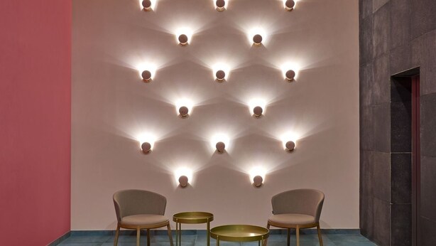 Un interno moderno con un lampadario geometrico a parete, due tavoli rotondi e due sedie.