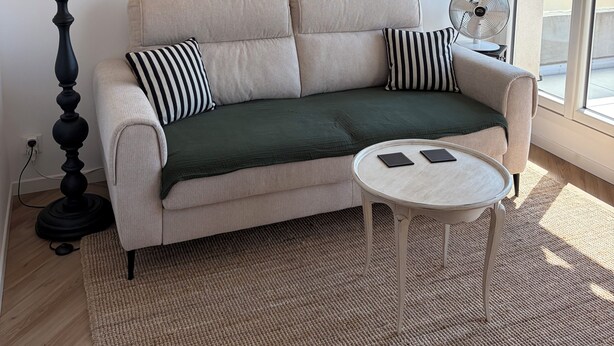 Un salon avec un canapé, un miroir rond, une lampe, un ventilateur et une petite table.