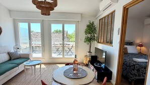 Un salon moderne avec une table ronde, des chaises rouges, un canapé et une grande fenêtre donnant sur un immeuble.