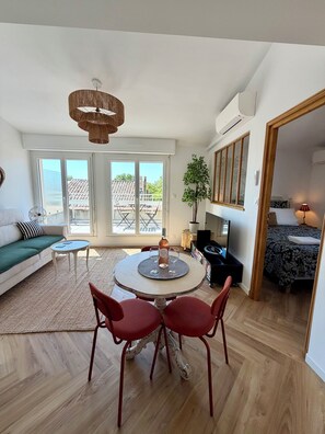 A modern living room with a round table, red chairs, a sofa, and a large window with a view of a building. - Stunning new apartment with 2 terraces and parking (Avignon)