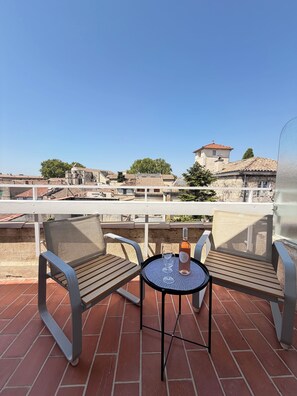Une terrasse avec deux chaises en bois et une table, une bouteille de vin et un verre posé sur la table.