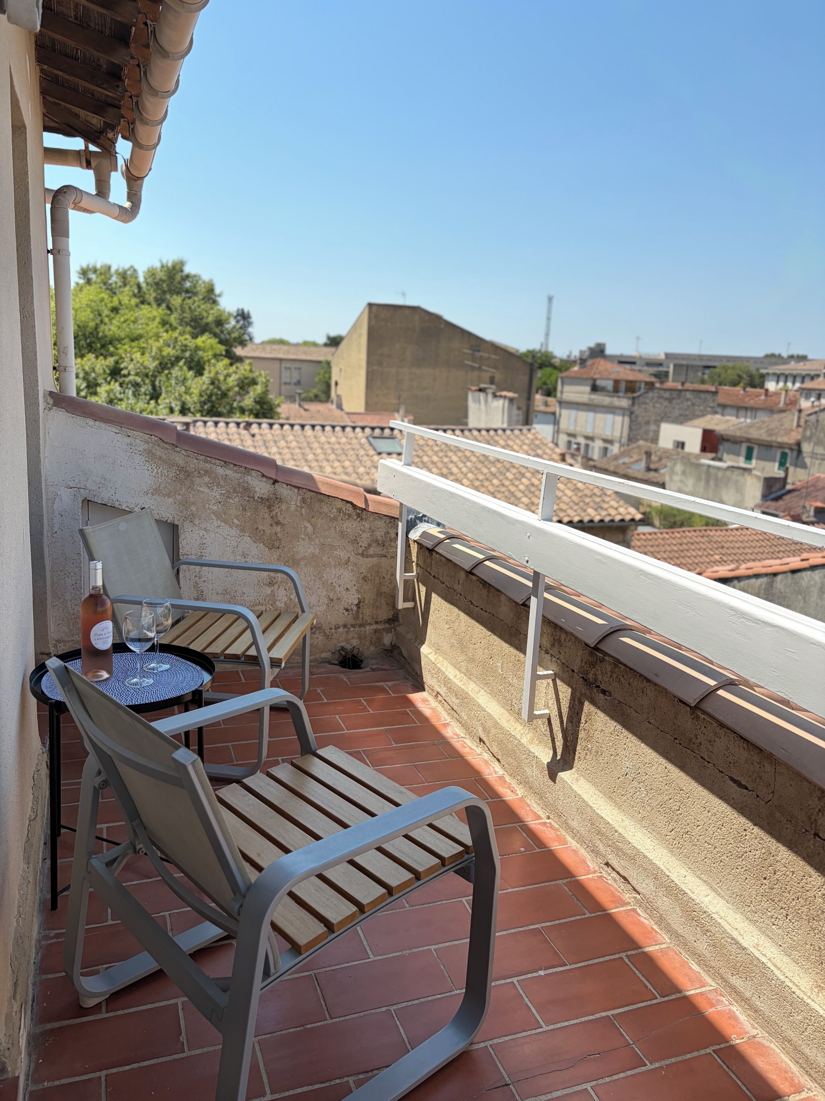 A balcony with a table and chairs, a bottle of wine, and a view of the cityscape.