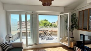 Un salon moderne doté d’une grande porte-fenêtre coulissante donnant sur une terrasse extérieure, d’une table basse ronde, d’un canapé et d’un téléviseur.