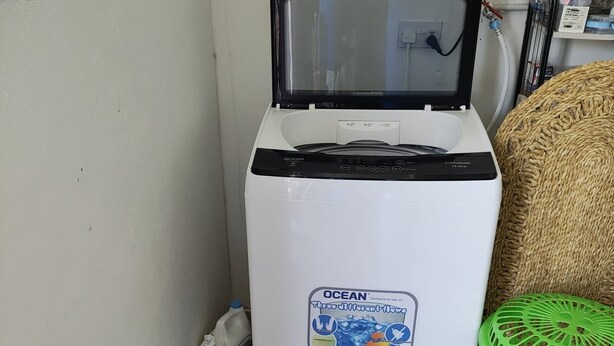 A compact refrigerator with a sticker indicating it has three different flows, next to a green laundry basket and cleaning supplies.