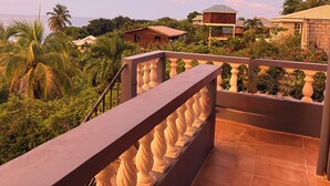 Uma varanda com guarda-corpo, vista para um jardim exuberante e um edifício com telhado em telhas.