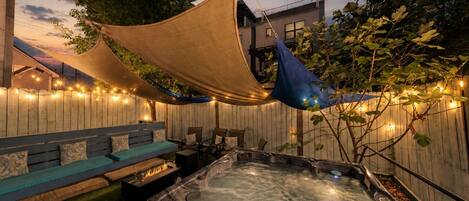 An outdoor patio with a hot tub, seating area, and string lights.