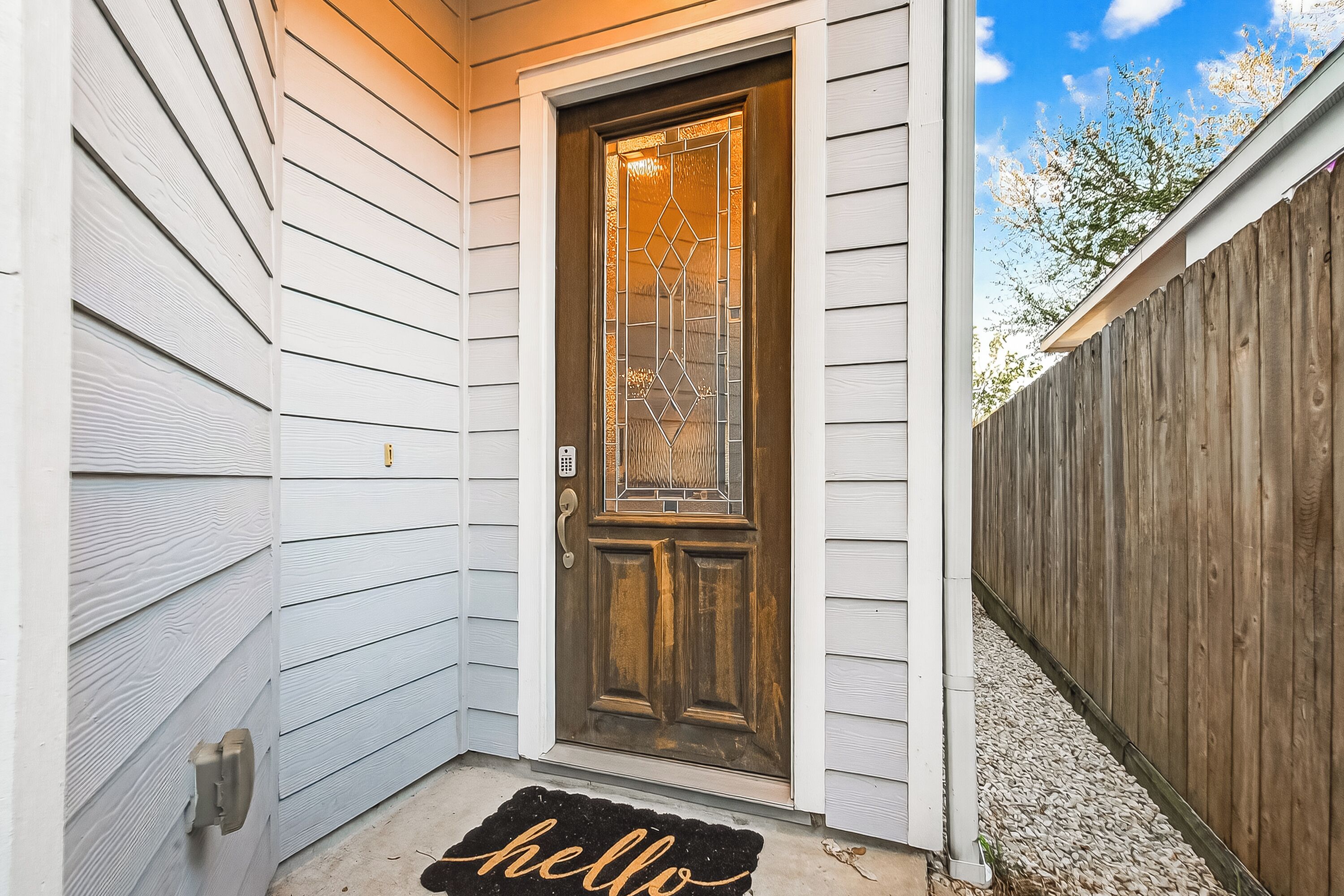 Una casa con puerta principal de madera, buzón y felpudo con la palabra 'hello'.