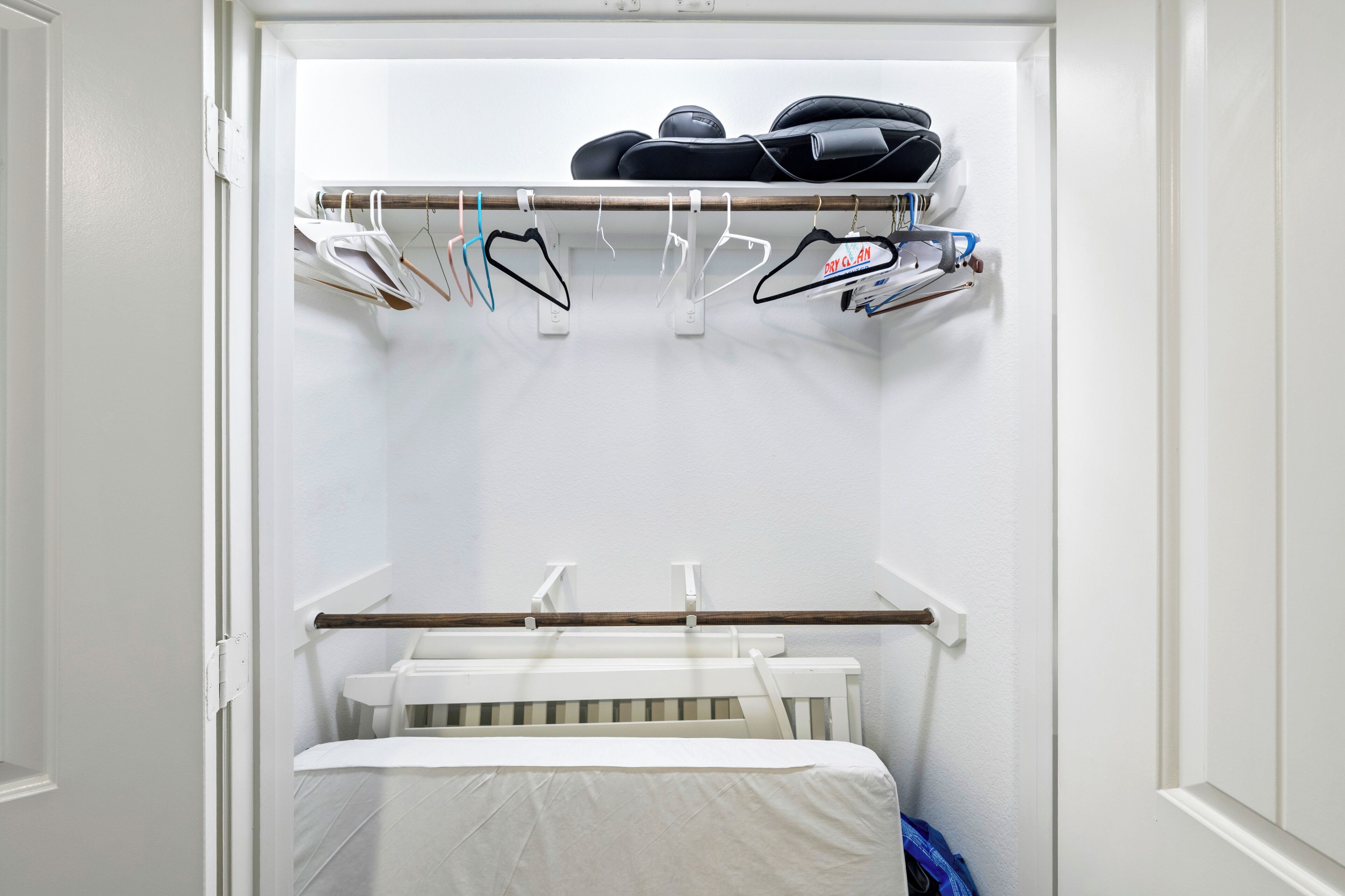 Un vestidor con una cuna blanca, ropa colgada y un zapatero.