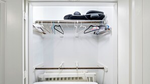 Ein begehbarer Kleiderschrank mit einem weißen Babybett, aufgehängter Kleidung und einem Schuhregal.