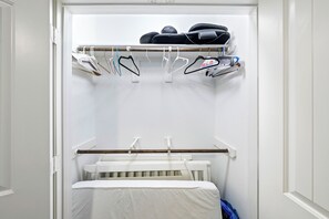 Ein begehbarer Kleiderschrank mit einem weißen Babybett, aufgehängter Kleidung und einem Schuhregal.