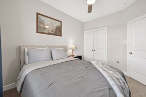 Ein Schlafzimmer mit einem Bett, einem Nachttisch, einer Lampe, einem gerahmten Bild und weißen Türen.