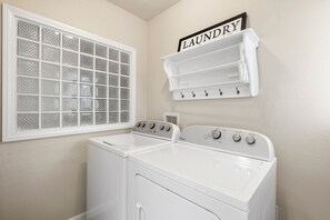 A laundry room with a white washing machine, a dryer, a window with a grid pattern, and a wall-mounted shelf with a 'laundry' sign. - Historic West Adams Area, Spanish-Style House (Los Angeles)