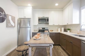 A modern kitchen with white cabinets, stainless steel appliances, and a wooden island. - Historic West Adams Area, Spanish-Style House (Los Angeles)
