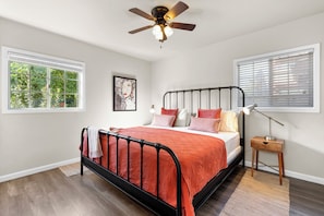 A bedroom with a bed, a ceiling fan, a window with blinds, a bedside lamp, and a small table. - Historic West Adams Area, Spanish-Style House (Los Angeles)