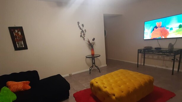 A living room with a black sofa, a yellow ottoman, a red rug, a small side table, and a television. - Lovely 3 Bedroom With Full sea View, Restaurants, (East London)
