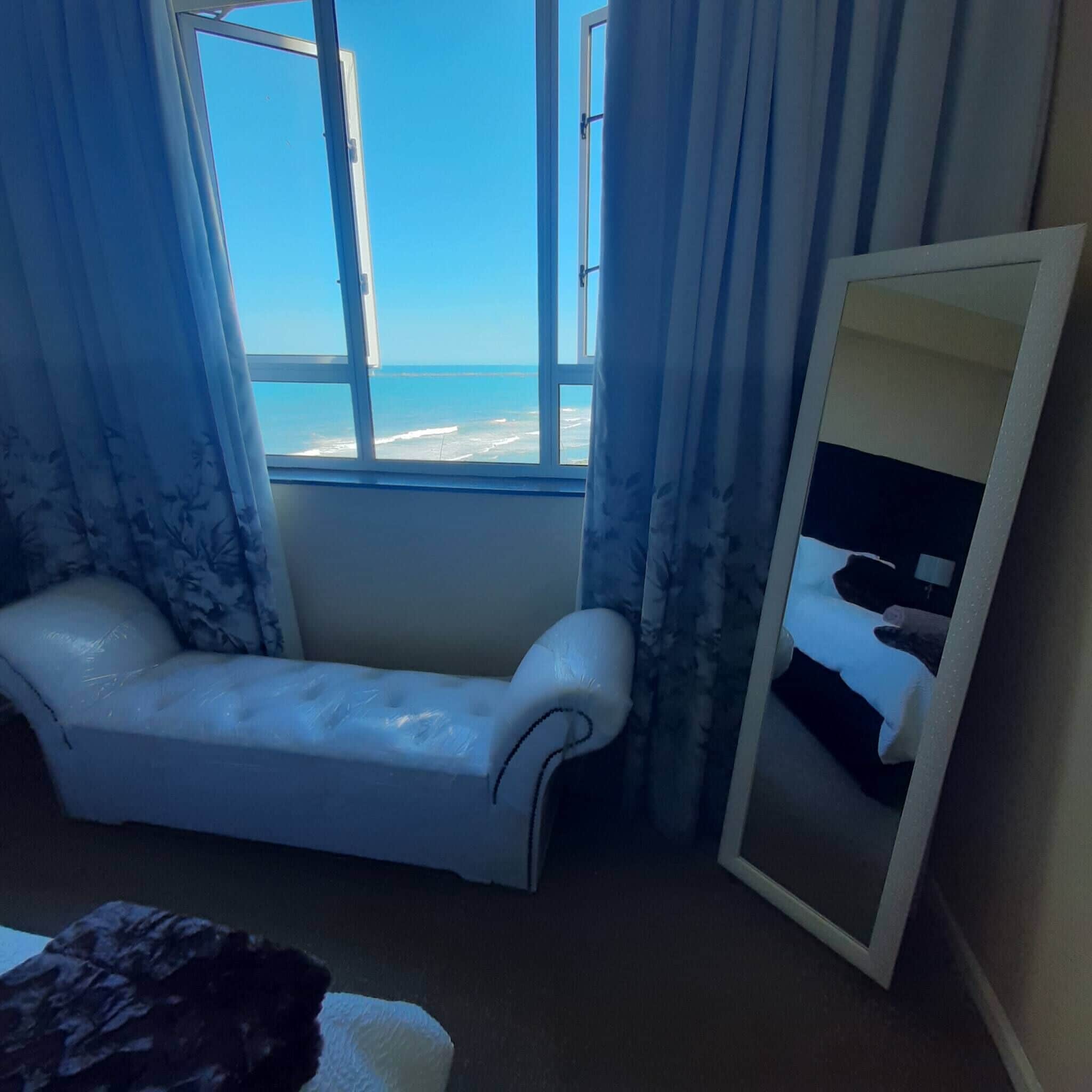Una habitación con vista al mar, un sofá blanco y un espejo.
