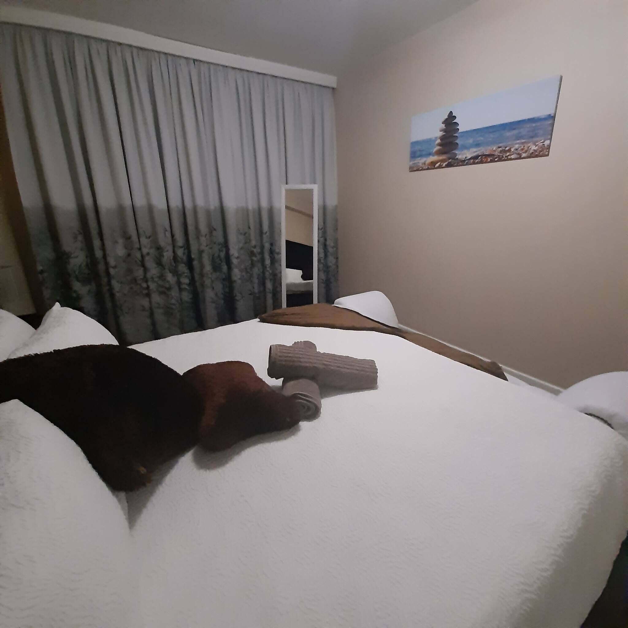 A hotel room with a bed, a window with curtains, a painting on the wall, and a wooden headboard.