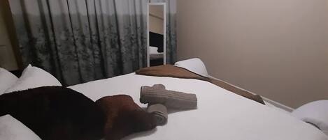 A hotel room with a bed, a window with curtains, a painting on the wall, and a wooden headboard.